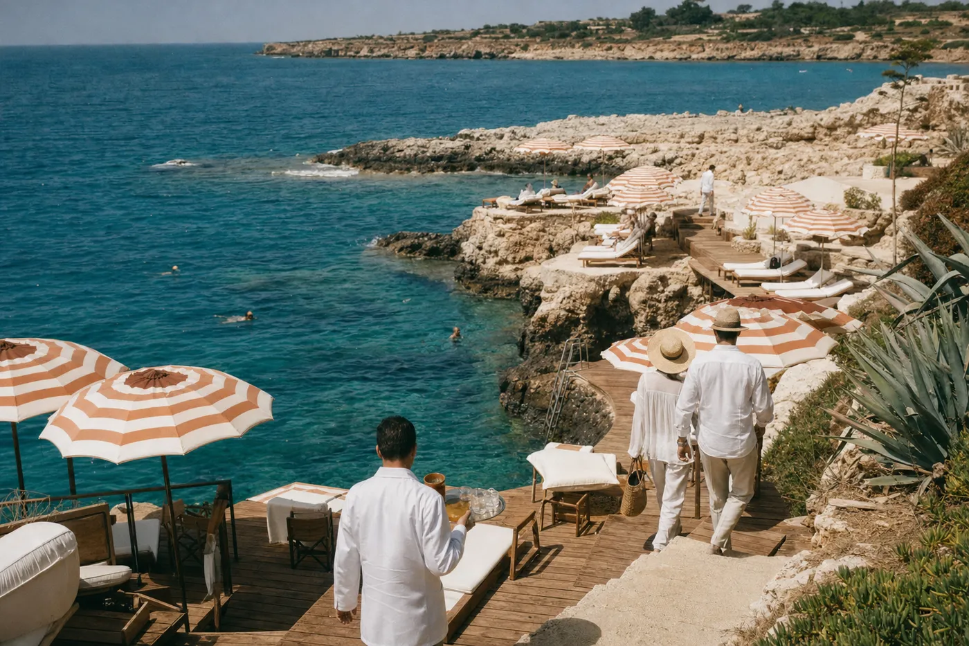 Striped umbrellas and white loungers on a rocky beach club above clear water