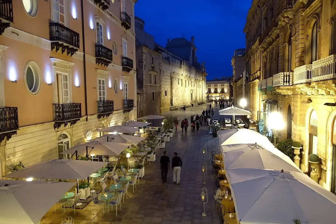 Tables out on a lit street in Ortigia at night