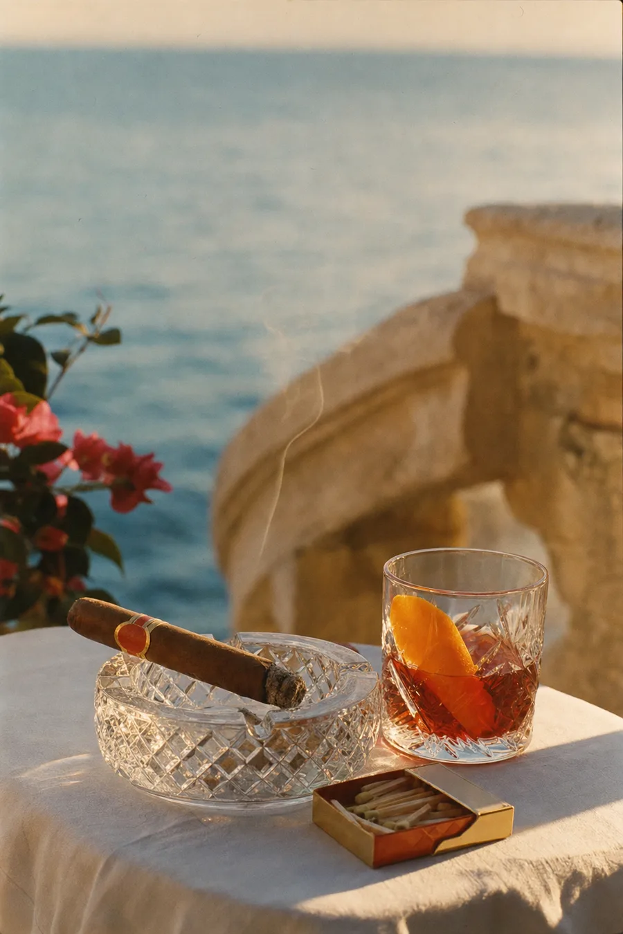 A cigar on a crystal ashtray beside a Negroni, on a terrace above the sea