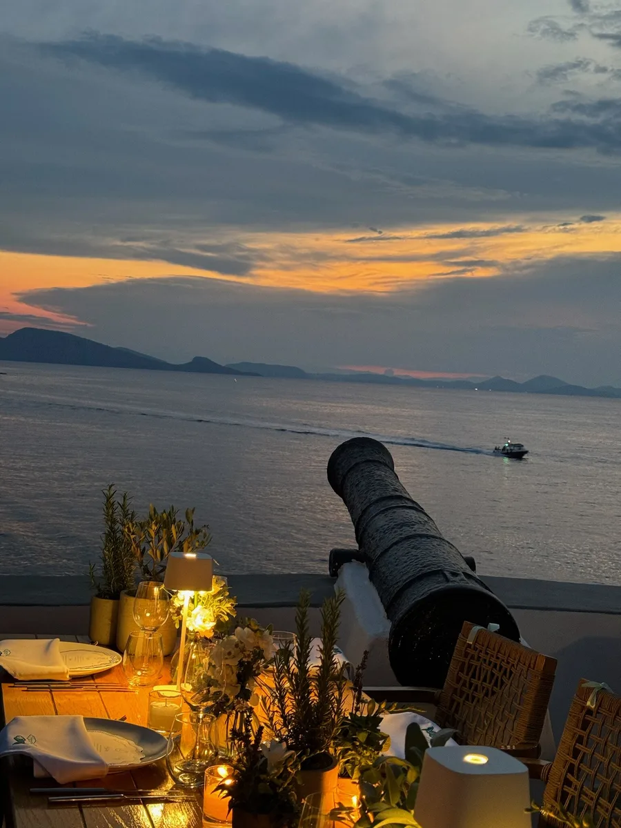 A table beside an old cannon above the sea at sunset